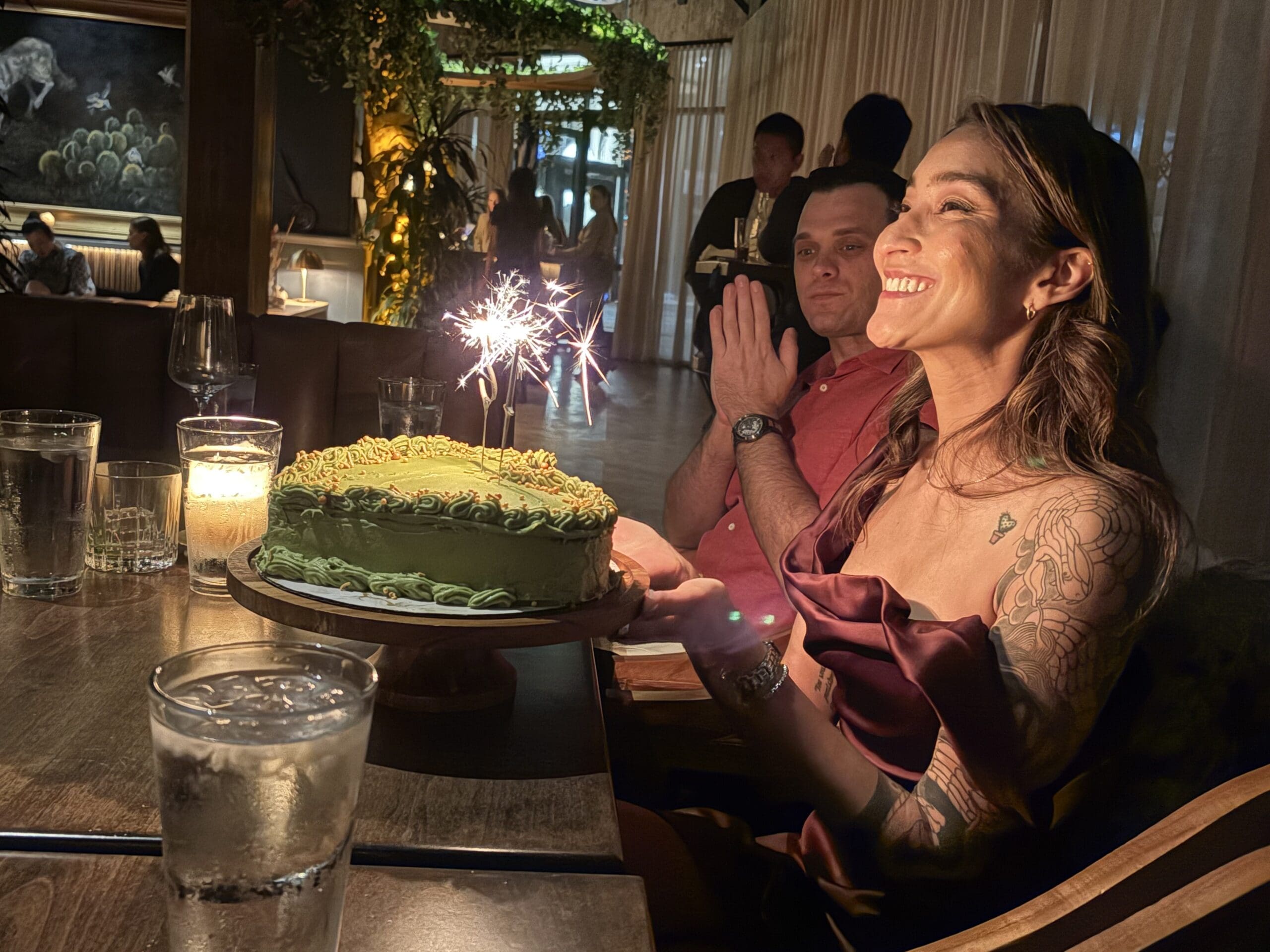 Photo of Taylor Nakakihara holding a green heart shaped birthday cake with lit sparklers