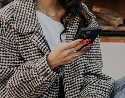woman with herringbone jacket and white shirt holding black iphone
