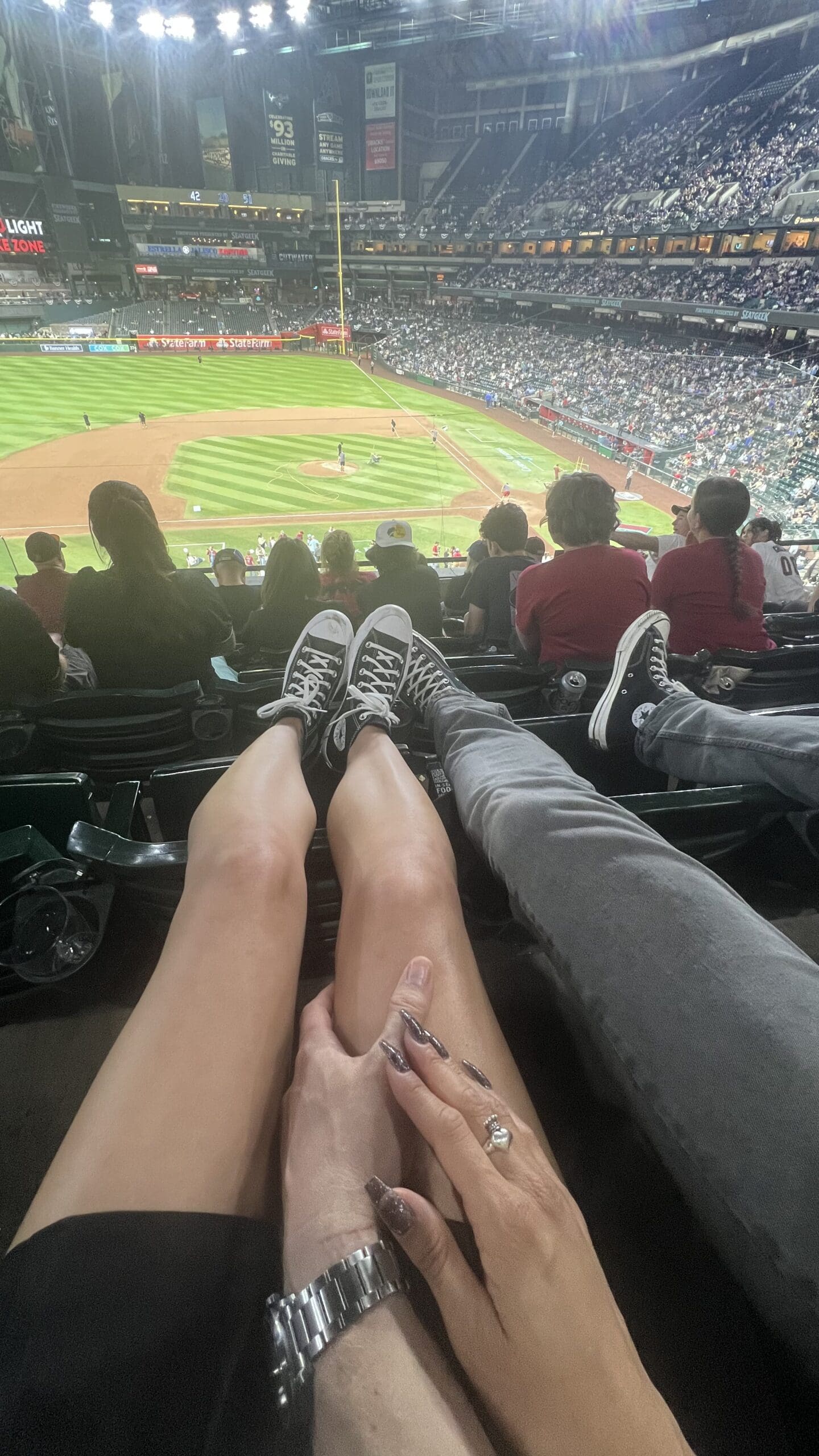 Two people holding hands wearing matching shoes at a baseball game